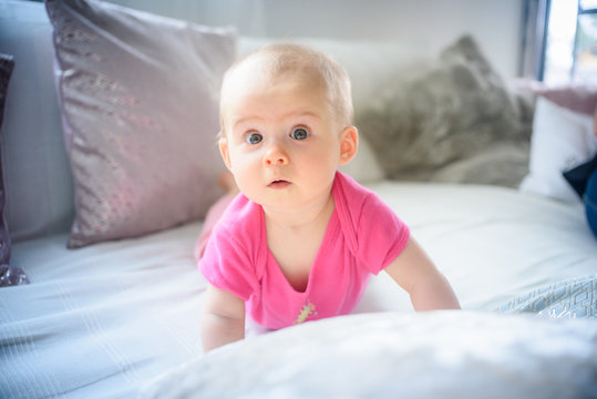 Sweet adorable baby girl lying on a couch looking towards camera. 6-7 months old infant on belly lifting upper body