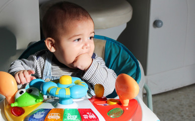 baby boy in the walker, puting his hand in mouth, growing teeth