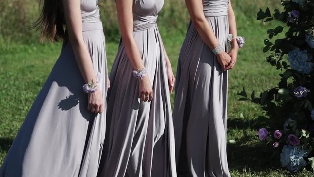 Bridemaids in blue gray dresses staying at wedding ceremony outdoors waving dresses at sunny summer day