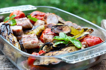 Juicy sausages and grilled vegetables in a glass bowl on a nature background. Dinner outdoors. Garden party.
