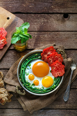 Sunny side fried eggs in a copper pan with tomatoes and green beans, copy space.