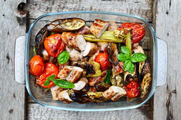 Juicy sausages and grilled vegetables in a glass bowl on a nature background. Dinner outdoors. Garden party. The top view
