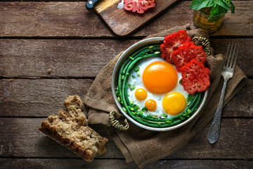Sunny side fried eggs in a copper pan with tomatoes and green beans, copy space.