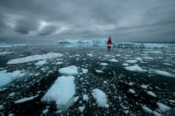 Greenland iceberg mirror panorama with red sail ship and heavy clouds 