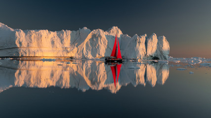 Greenland midnight Sunset iceberg mirror panorama with red sail ship 