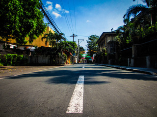 Perspective shot of a Manila city street road with trees and brightly painted buildings on a summer...
