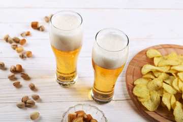 Two glass of beer and snacks on a white wooden table. Chips, pistachios, dry cheese.