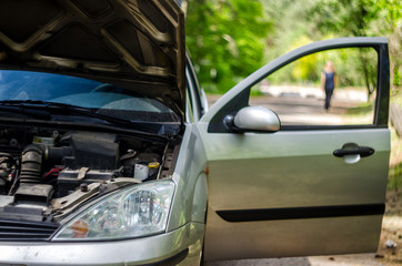 Obraz premium Broken car on the roadside with an open hood doors. Silhouette of a retreating driver, left a broken car concept