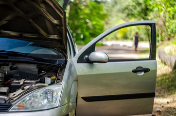 Broken car on the roadside with an open hood doors. Silhouette of a retreating driver, left a broken car concept