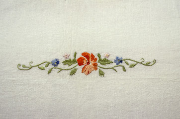 Embroidery on cotton fabric from floral ornament with orange-red flower,blue flowers and leaves on...