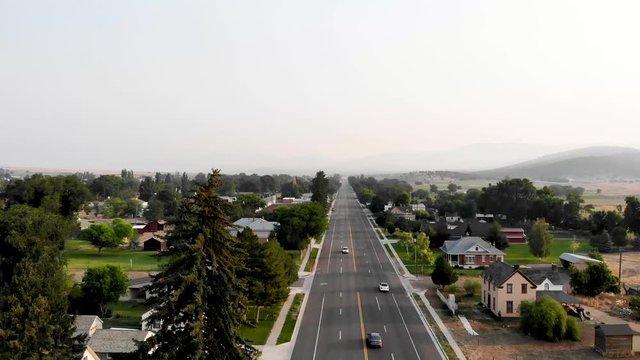 Aerial-Flying Over Main Street With Light Traffic In A Small Rural Mountain Town In The Golden Morning Light  With Smokey Haze On The Horizon From Wildfires In The Vicinity.