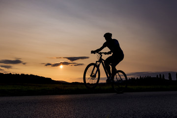 Silhouette of boy on the bike. Young cyclist is jumping on his bike during sunset. Fore wheel is over the horizon.