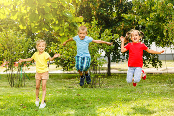 Naklejka na ściany i meble Three children at sunset jumping in the park