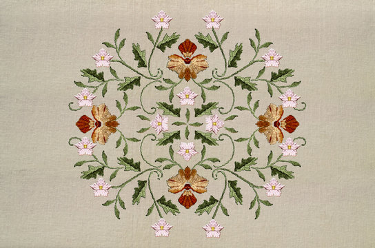 Oval embroidered pattern with red-yellow flower and pink flowers on twisted stems with leaves on cotton fabric


