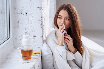 Fototapeta premium Beautiful young woman using nasal spray. Close up of female feeling sick nose using sinus medication for blocked nose. Healthcare and medical concept.
