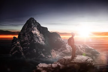 Fototapeten Silhouette of a hiker standing on a mountain peak © XtravaganT