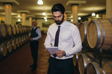 Winemakers in wine cellar holding glass of red wine and checking it. Sommeliers testing wines in...