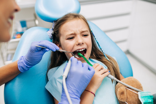 Cute little girl sitting on dental chair and having dental treatment.