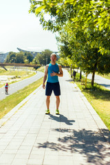 Fototapeta premium Man prepare to running on a track in a sunny day. Young couple working out in urban area.