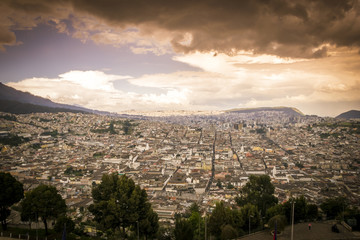 Obraz premium A panoramic view from higher ground of the city of Quito, capital of Ecuador. Buildings, houses and the mountains can be seen in the back. It's a sunny day with blue sky. photo taken from El Panecillo