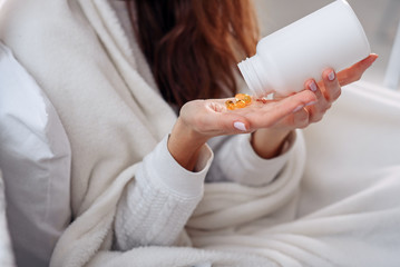 Vitamins and food supplements concept. Closeup of female hand pouring yellow pills out of bottle into palm. Woman spilling out medication, tablets, capsules on hand.