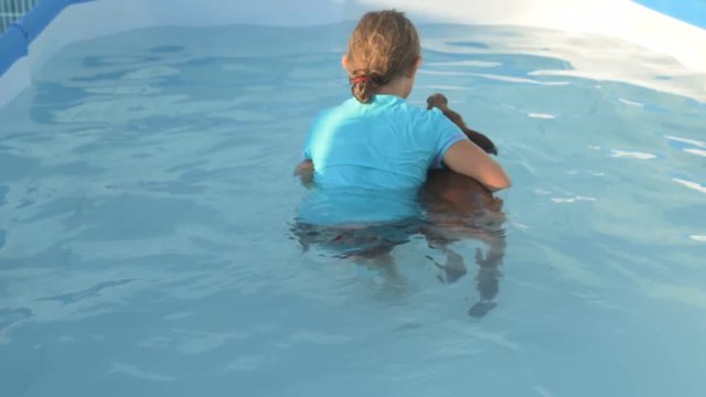 Young girl in bathing suit is swimming in clear, blue water of pool with red pig of Duroc breed. 2019 year of yellow pig. Concept of friendship between man and animals, respect for nature