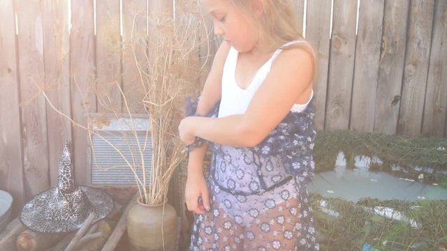 Young girl is preparing to take part in celebration of Halloween. Child is bathing in cauldron with chamomile flowers, trying on pointed hat. She is ready to fly on broomstick like a witch.