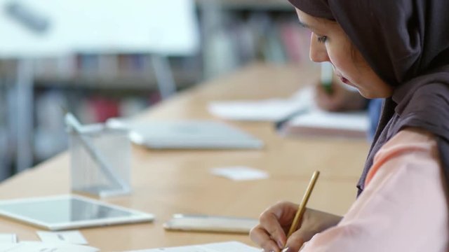 Close up of muslim woman in hijab marking correct answers in test while passing exam in university