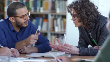 Close up of Caucasian female teacher leaning on table and speaking with middle eastern male student during lesson