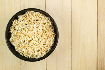 Instant noodles in a black bowl on wooden table