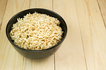 Instant noodles in a black bowl on wooden table