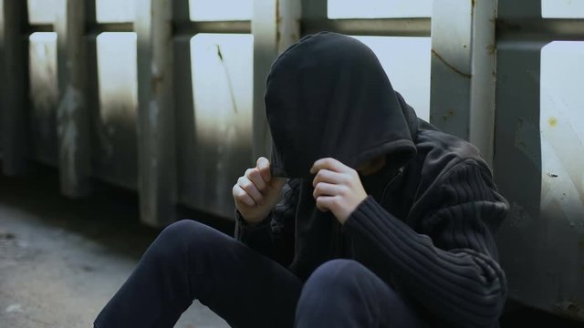 Miserable teenager wrapping in hood, going to sleep on street, depression crisis
