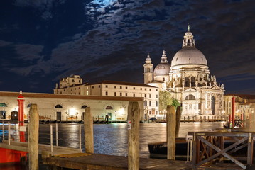 Night view of grand canal and its riverside and pier, Venetian Gothic architectures and background of Basilica di Santa Maria della Salute in Venice, Italy