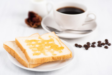 Sliced bread with honey topping and cup of black coffee on white table, delicious breakfast