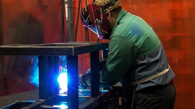 Gas Metal Arc Welding by worker in leopard skin hat with custom painted helmet in factory welding booth.