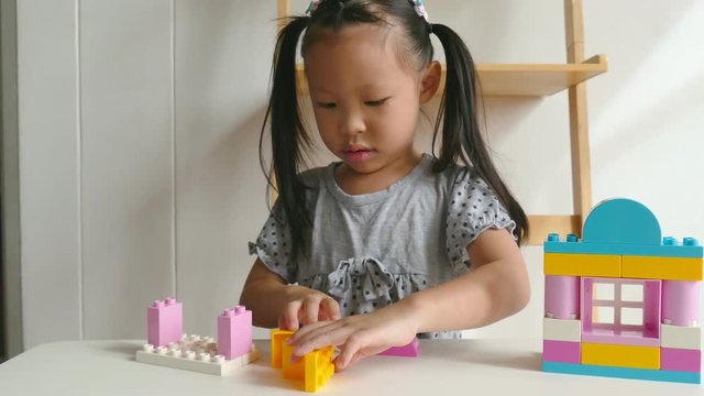 Young asian girl playing colorful plastic blocks at home