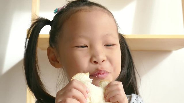Little asian girl eating bread for breakfast at home
