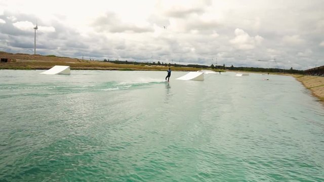 Young man wake boarding in the water park. Man with hydra costume, helmet. Blue water, cloudy day, summer.