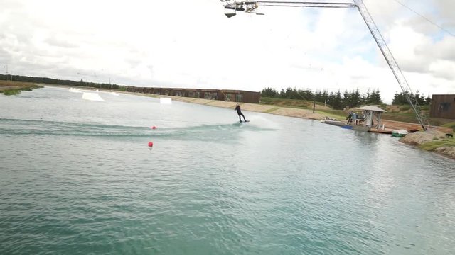 Young man wake boarding in the water park. Man with hydra costume, helmet. Blue water, cloudy day, summer.