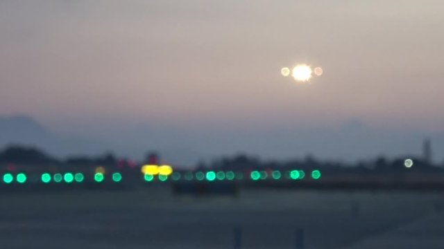 An aircraft approaching the runway with all the lights on during the sunset. Unfocused and blurry on purpose. May 2018. Alicante airport.