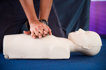 Hands of a man practicing CPR on mannequin in first aid class.