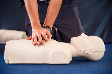 Hands of a man practicing CPR on mannequin in first aid class.
