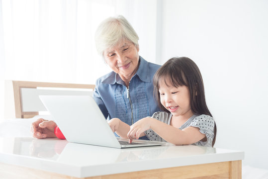 Little asian girl playing games on laptop computer with her grandmother