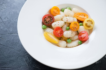 Potato gnocchi served with fresh cherry tomatoes and green peas in a white plate, selective focus, horizontal shot