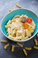Bowl of fusilli with tomatoes and cheese over grey stone background, studio shot