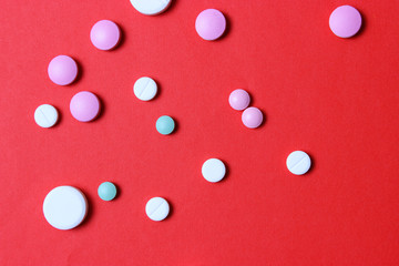 Colorful pills of different sizes on a red background.
