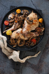 Roasted rabbit with champignon mushrooms and cherry tomatoes, high angle view, studio shot