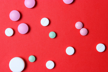 Colorful pills of different sizes on a red background.