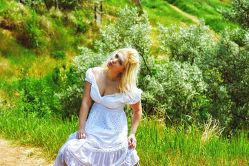 Portrait of a young woman in a white dress in nature . Blonde girl on a walk outside the city