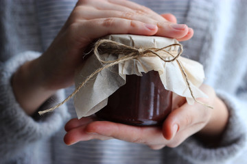 chocolate paste in a bank in female hands on a light background.